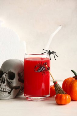 Cadılar Bayramı kutlaması için arka planda bir bardak lezzetli kırmızı kokteyl, kafatası ve balkabağı.