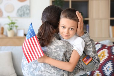 Amerikan bayrağı taşıyan küçük bir çocuk askeriyede annesine sarılıyor.