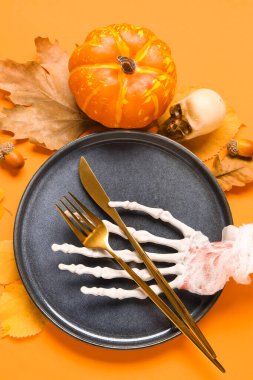 İskelet elli Cadılar Bayramı sofrası ve turuncu arka planda sonbahar dekoru.