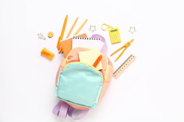 Beyaz arka planda farklı kırtasiye malzemeleriyle süslü okul çantası.