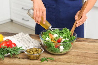 Mutfaktaki masada lezzetli salata ile zeytinyağı ekleyen bir kadın.