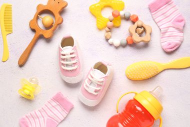 Stylish baby shoes with socks, rattles, brushes, bottle of milk and pacifier on grunge white background clipart