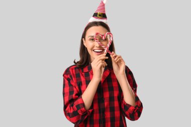 Pijamalı güzel bir kadın ve gri arka planda şeker kamışlı Noel Baba şapkası.