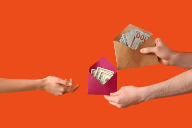 Turuncu zemin üzerinde para olan zarfları tutan eller.