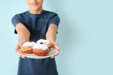 Kipa 'lı küçük çocuk elinde lezzetli donutlarla mavi arka planda bekliyor. Hanuka kutlaması