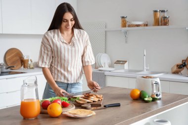 Genç ve güzel bir kadın mutfakta reçel ve fıstık ezmesi ile lezzetli tost yapıyor.