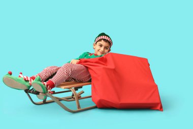 Mavi arka planda kızağı ve hediye çantası olan sevimli küçük bir elf.