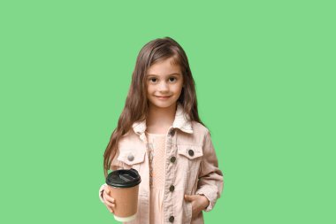 Yeşil arka planda bir fincan kahveyle şık giyinmiş şirin küçük bir kız.
