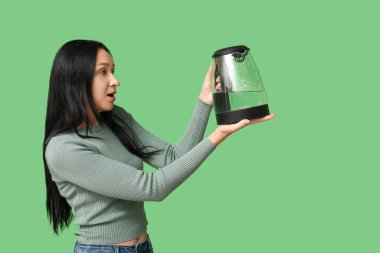 Yeşil arka planda modern elektrikli su ısıtıcısı olan güzel genç bir kadın.