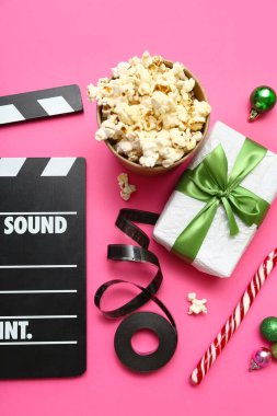 Patlamış mısır, film makarası ve pembe arka planda Noel dekoru olan bir film.