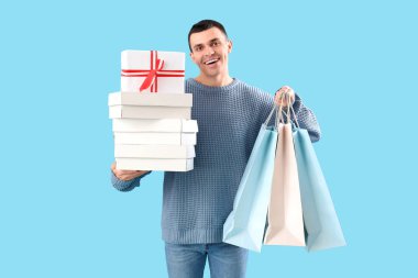 Mavi arka planda hediye kutuları ve alışveriş çantaları olan yakışıklı genç adam.