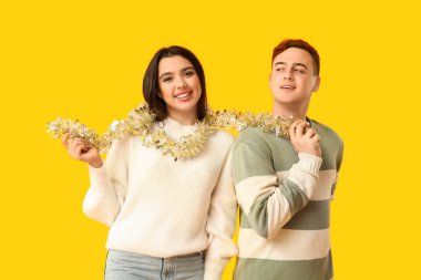 Sarı arka planda Noel süsleri olan genç bir çift.