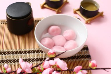 Pembe arka planda bir kase tangyuan ve sakura içeren bambu hasırı, yakın plan. Dongzhi Festivali