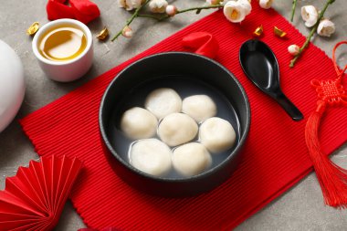 Gri grunge arka planında bir kase tangyuan ve Çin dekoru olan kırmızı hasırlar, yakın plan. Dongzhi Festivali