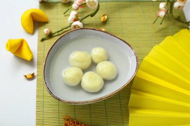 Beyaz arka planda bir kase tangyuan ve Çin dekorlu bambu hasırı, yakın plan. Dongzhi Festivali