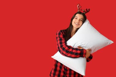 Kareli pijamalı ve kırmızı arka planda yumuşak yastıklı ren geyiği boynuzlu güzel bir kadın.