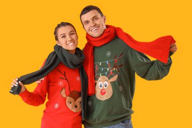 Sarı arka planda eşarpları olan Noel süveteri giyen genç bir çift.