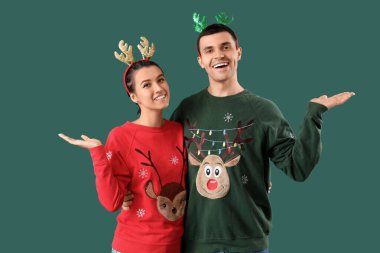 Noel süveterleri ve yeşil arka planda ren geyiği boynuzları olan genç bir çift.