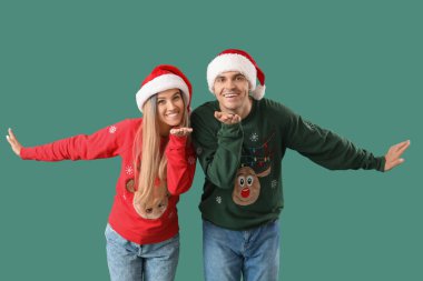 Noel Baba şapkalı ve Noel kazaklı genç çift yeşil arka planda öpüşüyorlar.