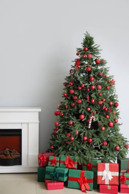 Süslü Noel ağacı, hediye kutuları ve beyaz duvarın yanındaki şömine.