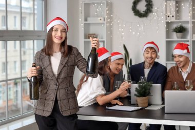 Ofisteki şirket partisinde elinde şampanya şişeleriyle yeni yılı kutlayan genç bir kadın.