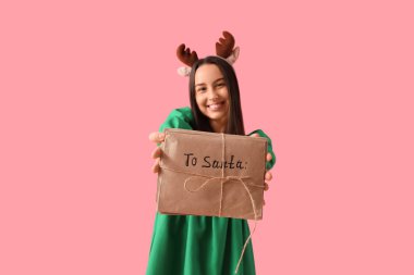 Geyik boynuzları takmış güzel bir kadın pembe arka planda Noel Baba 'ya mektuplar yazıyor.