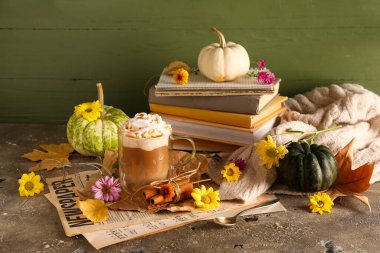 Bir bardak lezzetli balkabaklı latte, tarçınlı, kitaplı ve güzel çiçekli gri masa.