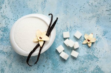 Aromatik vanilya şekerli kase, çiçekler ve mavi arka planda çubuklar