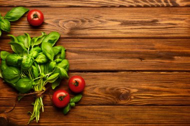 Taze yeşil fesleğen ve ahşap zemin üzerinde domatesler.