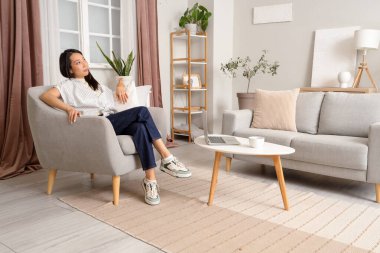 Young Asian woman sitting in armchair at home