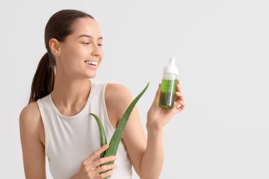 Bitki yaprağı ve beyaz arka planda bir şişe aloe vera spreyi olan güzel, mutlu genç bir kadın.