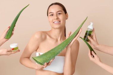 Bitki yaprakları ve elleri bej arka planda aloe veradan yapılmış kozmetik ürünler tutan güzel, genç ve mutlu bir kadın.