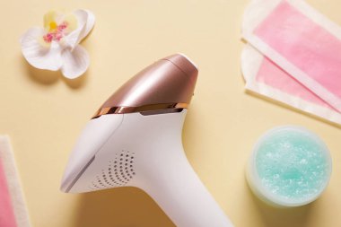 Balmumu şeritli modern fotoepilatör, sarı arka planda bir kavanoz fırça ve orkide çiçeği.