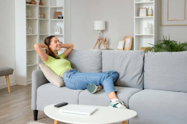 Oturma odasındaki gri kanepede dinlenen genç kadın.