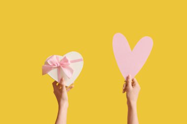 Kağıt kalpli kadın eller ve sarı arka planda hediye kutusu. Sevgililer Günü kutlaması