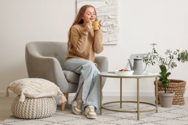Bir fincan çayla evdeki koltukta oturan genç bayan.
