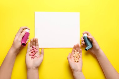 Sarı arka planda çocuk elleri, haplar ve astım spreyleri.