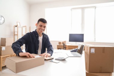 Depodaki masada müşteriler için paket paketleyen bir erkek çevrimiçi mağaza satıcısı