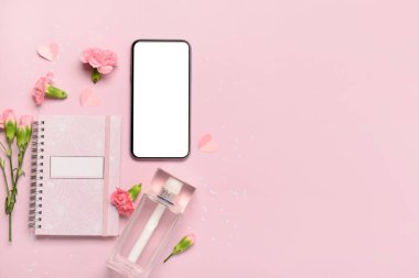 Modern cep telefonlu kompozisyon, bir şişe parfüm ve pembe arka planda karanfil çiçekleri.
