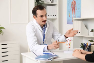 Omurga modelini klinikteki hastaya açıklayan erkek doktor.
