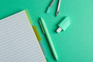 Yeşil arka planda açık defter, pusula, silgi ve kalemle kompozisyon. Üst görünüm