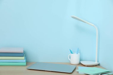 Mavi duvarın yanında kitapları ve dizüstü bilgisayarı olan şık bir iş yeri