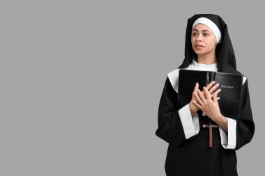 Gri arka planda İncil 'i olan genç rahibenin portresi