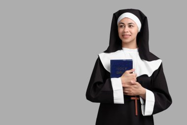 Gri arka planda İncil 'i olan genç rahibenin portresi