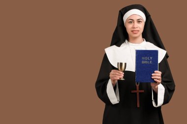 Kahverengi arka planda İncil ve kadehi olan genç rahibe.