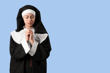 Mavi arka planda dua eden genç bir rahibe