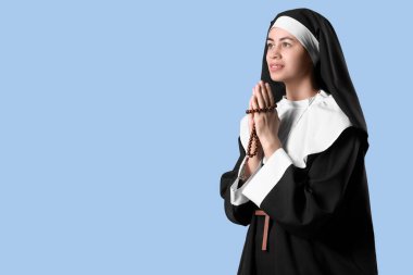 Mavi arka planda dua eden tespih taşıyan genç bir rahibe.