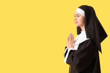 Genç rahibe sarı arka planda dua ediyor.