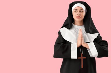 Genç rahibe pembe arka planda dua ediyor.