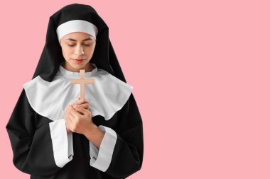 Pembe arka planda haç çizen genç rahibe